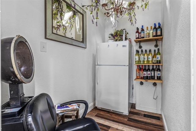 interior space with a textured wall, wood finished floors, freestanding refrigerator, and baseboards