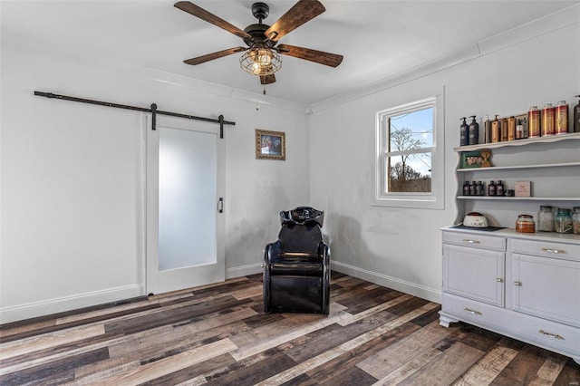 living area featuring a barn door, baseboards, a ceiling fan, dark wood-style flooring, and crown molding