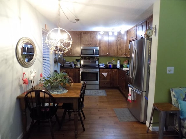 kitchen with a chandelier, stainless steel appliances, wood finished floors, dark countertops, and pendant lighting