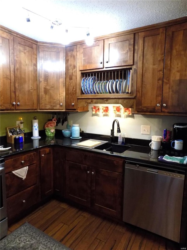 kitchen featuring dark countertops, stainless steel dishwasher, dark wood-type flooring, a sink, and a textured ceiling