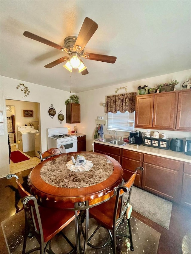 kitchen featuring washer and clothes dryer, brown cabinets, white gas range, light countertops, and a sink