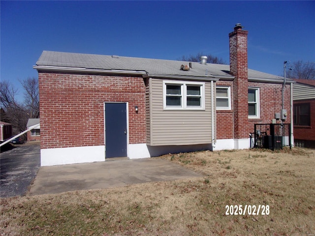 back of house featuring a lawn, brick siding, and a chimney