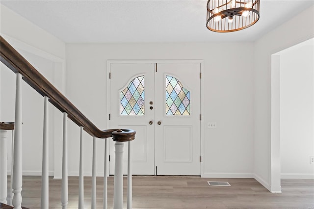 foyer featuring visible vents, an inviting chandelier, light wood-type flooring, baseboards, and stairs