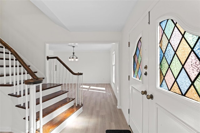 entrance foyer with baseboards, stairway, light wood-style flooring, and a notable chandelier