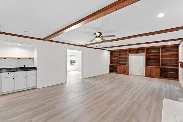 unfurnished living room with light wood-style floors, a ceiling fan, baseboards, and beamed ceiling