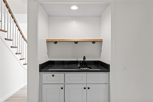 bar featuring light wood-style flooring, a sink, and stairway