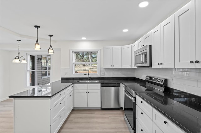 kitchen with a peninsula, a sink, appliances with stainless steel finishes, decorative backsplash, and light wood finished floors