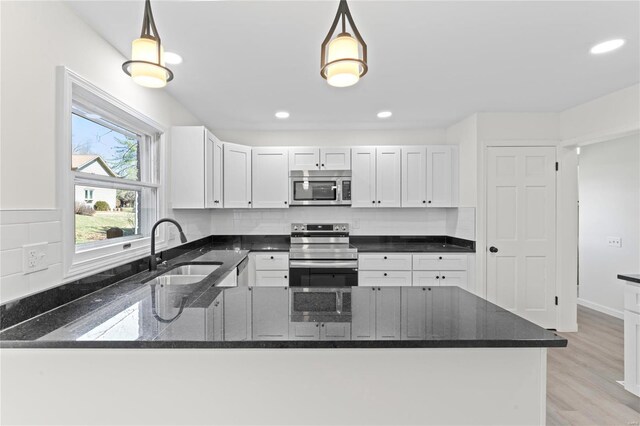 kitchen with white cabinets, appliances with stainless steel finishes, dark stone countertops, a sink, and backsplash