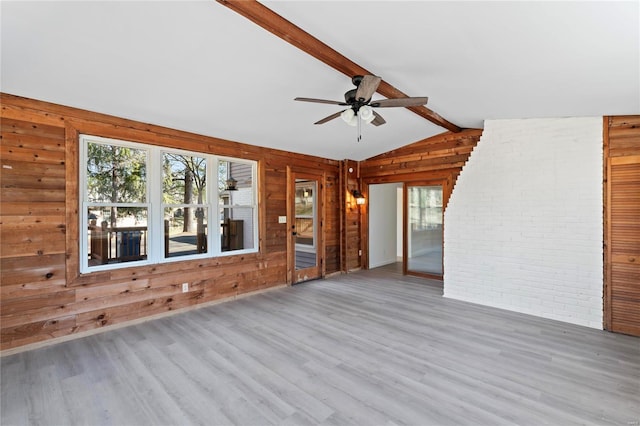 unfurnished living room featuring vaulted ceiling with beams, wood walls, ceiling fan, brick wall, and wood finished floors