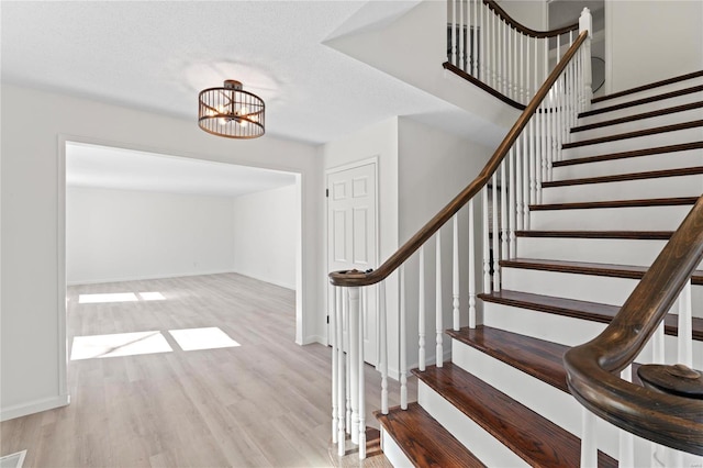 stairway with a textured ceiling, baseboards, a chandelier, and wood finished floors