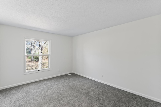 spare room featuring baseboards, visible vents, dark carpet, and a textured ceiling