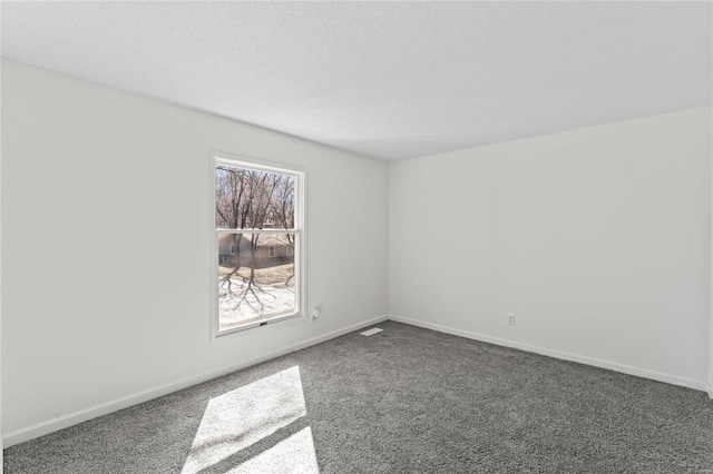 empty room with a textured ceiling, dark colored carpet, and baseboards