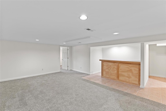 finished below grade area with light carpet, light tile patterned floors, visible vents, and recessed lighting