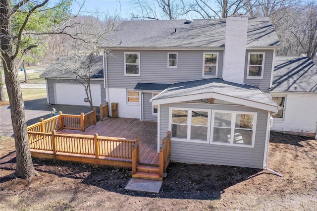 rear view of property featuring a shingled roof, driveway, a chimney, and a wooden deck