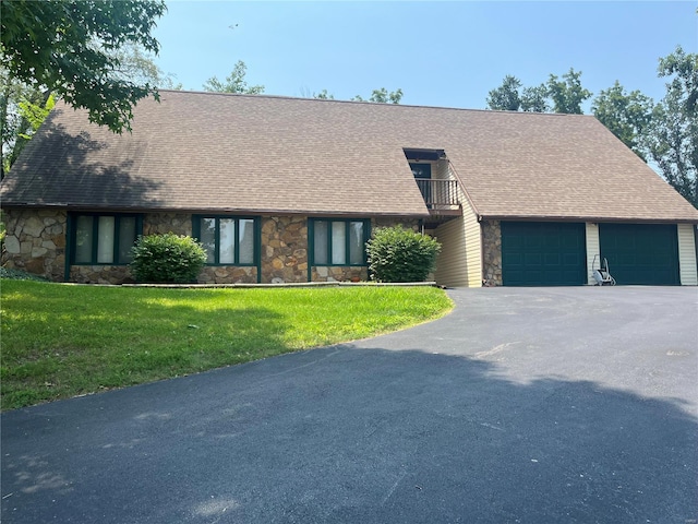 view of front of house with driveway, a balcony, stone siding, an attached garage, and a front yard