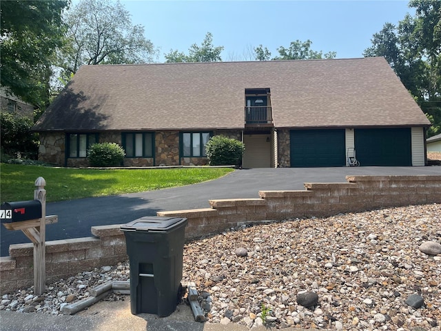 view of front of house featuring aphalt driveway, an attached garage, a front yard, a balcony, and stone siding