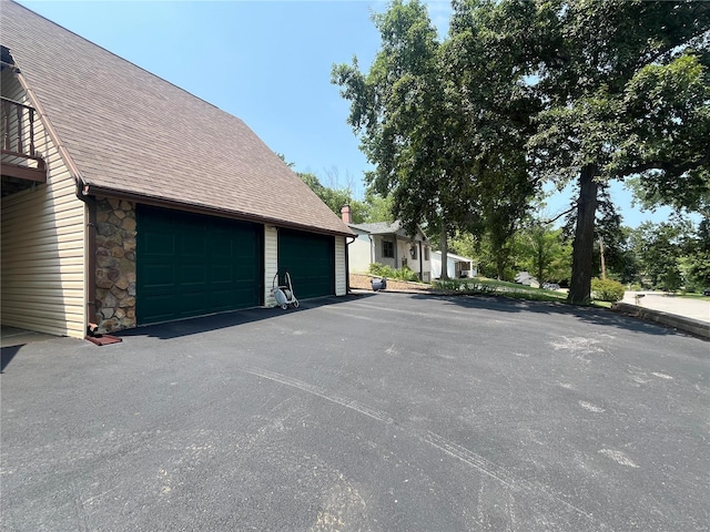 view of home's exterior with a garage, stone siding, and a shingled roof