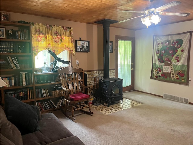 living area featuring carpet, visible vents, a ceiling fan, a wood stove, and wooden ceiling