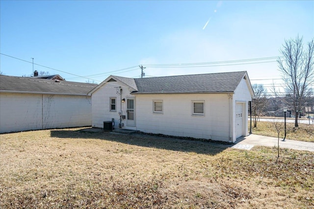 back of house with a shingled roof, cooling unit, and a yard