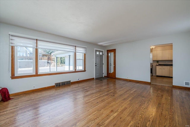 unfurnished living room featuring visible vents, baseboards, and wood finished floors