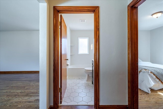 hall with visible vents, baseboards, and wood finished floors