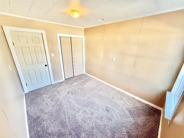 unfurnished bedroom with carpet floors, a closet, crown molding, and baseboards