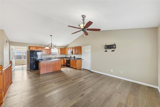 kitchen featuring baseboards, dark countertops, dark wood-style floors, a center island, and black appliances