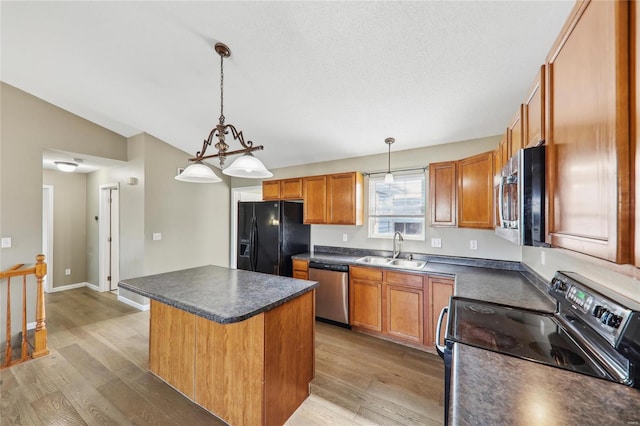 kitchen featuring a sink, a center island, black appliances, light wood finished floors, and dark countertops