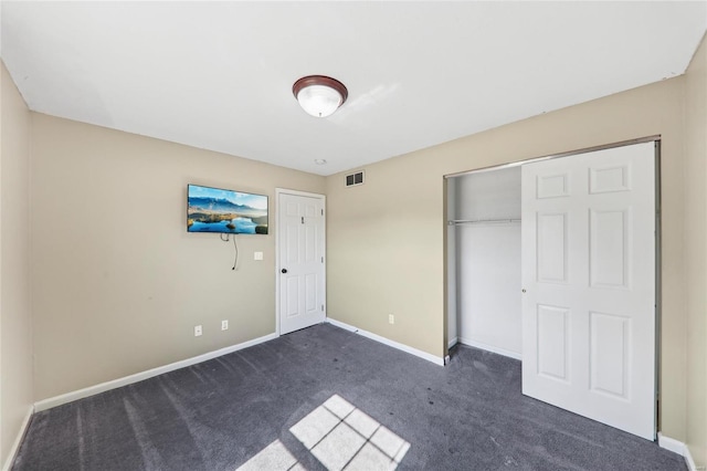 unfurnished bedroom with baseboards, visible vents, dark carpet, and a closet