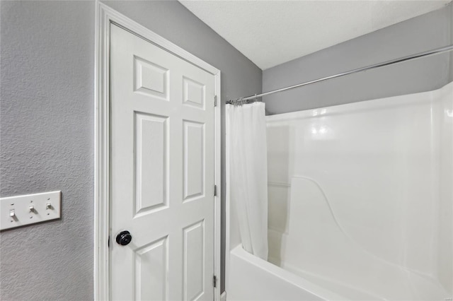 bathroom with shower / bathtub combination with curtain and a textured wall