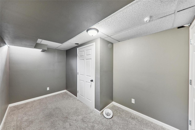 finished below grade area featuring a paneled ceiling, carpet, and baseboards