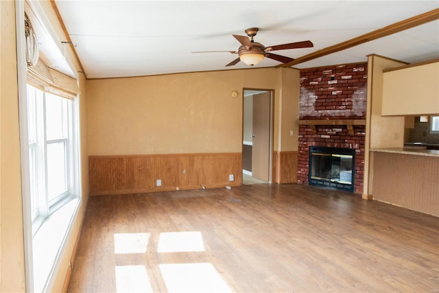 unfurnished living room with a wainscoted wall, wood finished floors, wooden walls, a fireplace, and ceiling fan