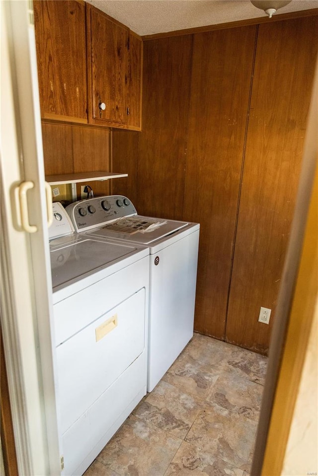 clothes washing area featuring washer and dryer, cabinet space, and wood walls