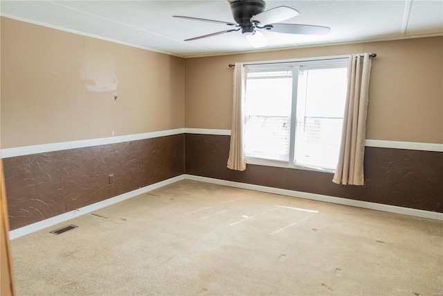 carpeted spare room featuring ornamental molding, baseboards, visible vents, and ceiling fan