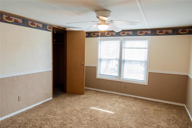 carpeted spare room with baseboards, ceiling fan, and a textured wall