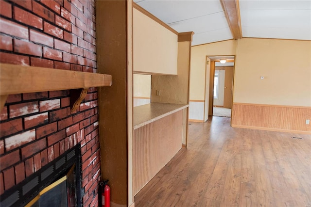 hall with a wainscoted wall, vaulted ceiling with beams, and hardwood / wood-style flooring