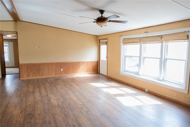 empty room with hardwood / wood-style flooring, a wainscoted wall, wood walls, and ceiling fan