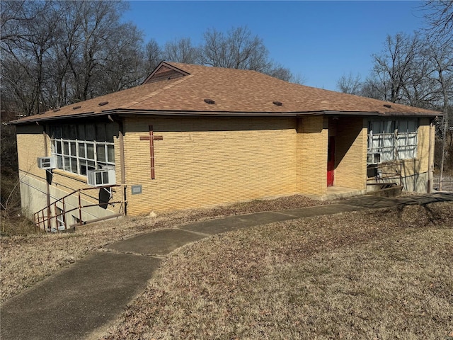 view of property exterior featuring a shingled roof, cooling unit, and brick siding