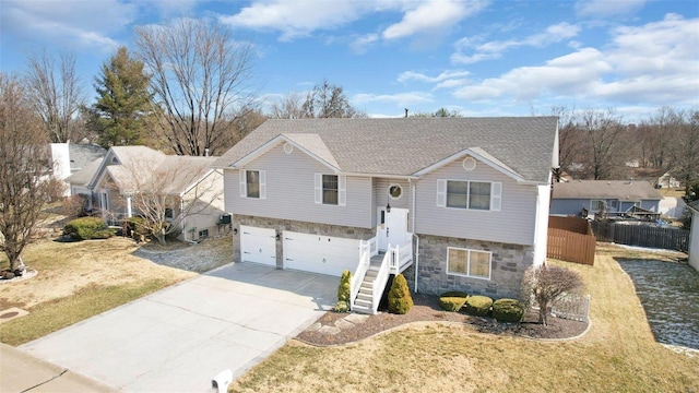 split foyer home featuring stairway, fence, a garage, stone siding, and driveway