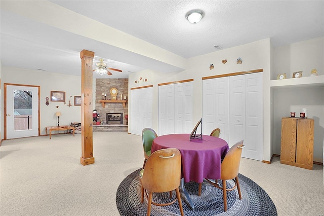 dining room featuring a textured ceiling, a stone fireplace, visible vents, and light colored carpet