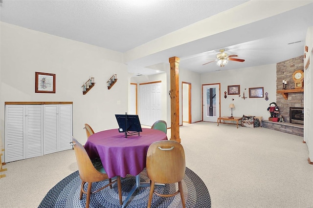 dining space featuring a textured ceiling, carpet floors, a stone fireplace, and decorative columns