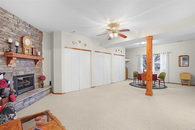 living area featuring carpet flooring, a stone fireplace, and a textured ceiling