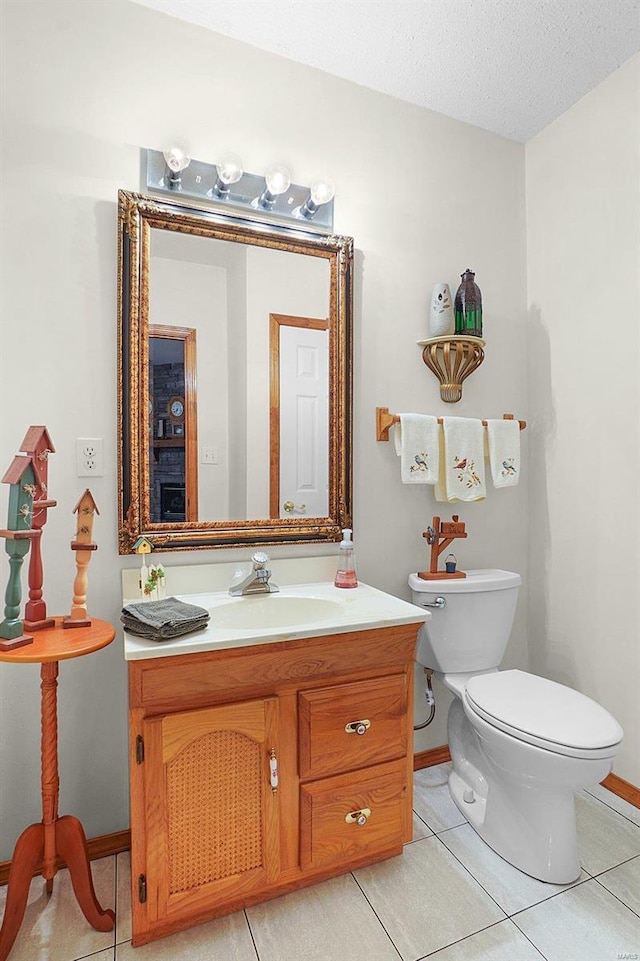 bathroom with a textured ceiling, tile patterned flooring, toilet, vanity, and baseboards