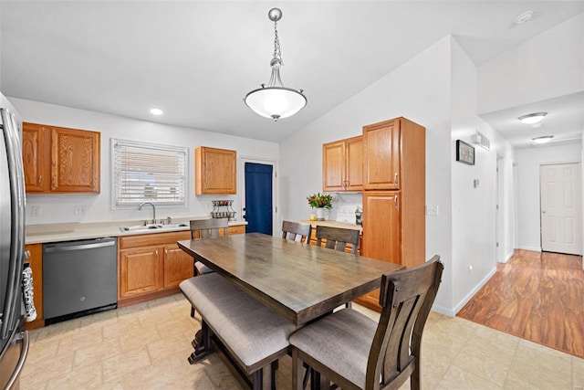 kitchen with a sink, baseboards, vaulted ceiling, stainless steel dishwasher, and brown cabinetry