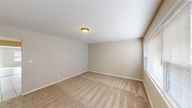 empty room featuring baseboards, light tile patterned flooring, and light colored carpet