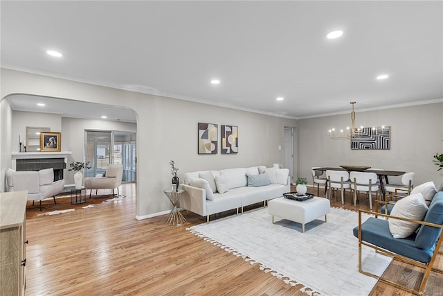 living room featuring arched walkways, crown molding, a fireplace, recessed lighting, and light wood-style floors