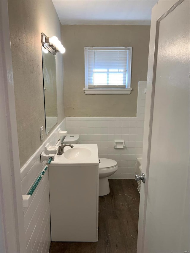 bathroom featuring tile walls, toilet, wainscoting, vanity, and wood finished floors