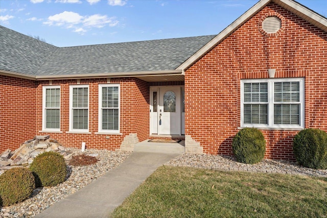 doorway to property with roof with shingles and brick siding