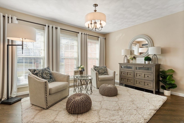 sitting room with a chandelier, dark wood-type flooring, and baseboards