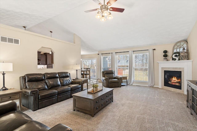 living area featuring light carpet, visible vents, a ceiling fan, a glass covered fireplace, and lofted ceiling